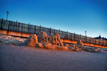 Sand castle on empty beach. Background with empty coastline at sunset.