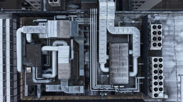 Aerial view of an industrial rooftop showcasing HVAC systems, vents, and piping, with snow covering parts of the surface in a winter setting.