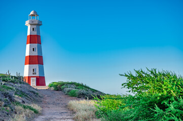 A lighthouse is on a hill with a clear blue sky