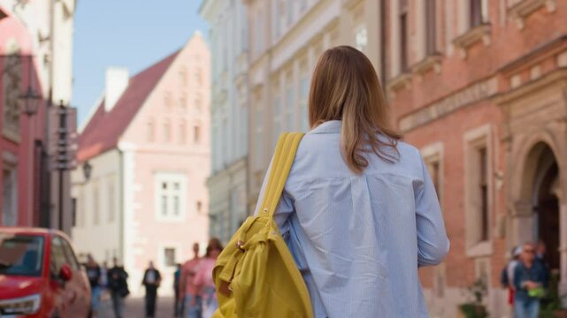 Woman carrying yellow backpack walking in Krakow, Poland. Female tourist exploring European city streets in summer day