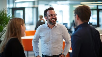 A man laughing and chatting with colleagues in a lively office space, exuding a fun and supportive work environment.