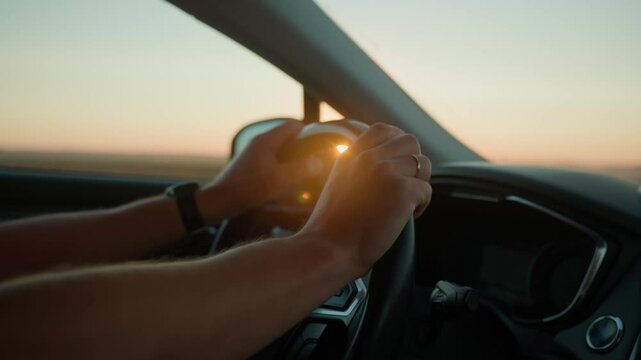 Male driver driving car, inside view. Man driving car on highway road at sunrise. Close-up of driver hands turning steering wheel