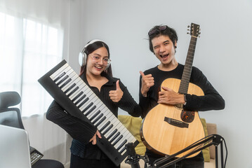 Two Professional Music Composer and songwriter composing a song with acoustic guitar, piano keyboard, drum pad and condenser microphone together at digital recording home studio.
