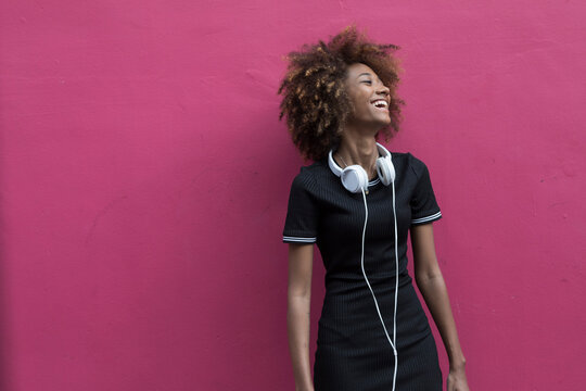 Happy woman standing with headphones in front of pink color wall
