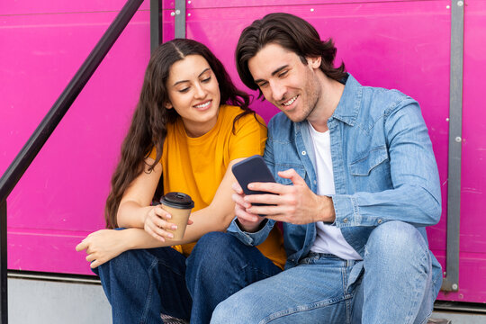 Smiling man sharing smart phone with woman having coffee on steps