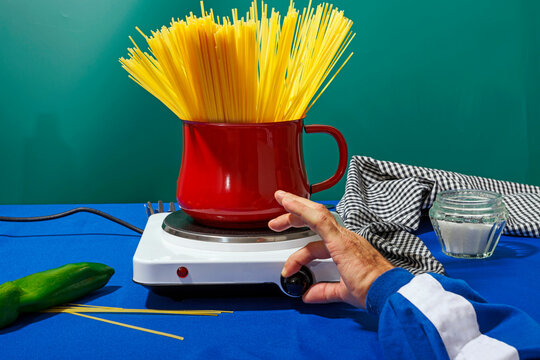 Hand of man adjusting gas stove button and cooking spaghetti in studio