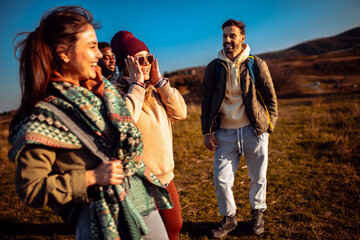 Smiling group of friends having fun while hiking together on hill at sunset.