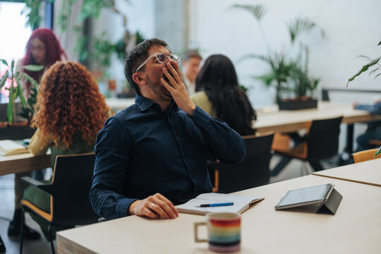 Tired office worker yawning during business meeting