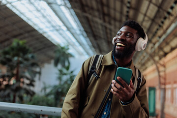 Tourist listening to music on his smart phone and smiling at the station