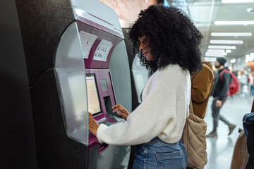 Young black woman buying train ticket at self-service kiosk in subway station