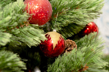 Christmas ornaments hanging on a lush green pine branch, symbolizing the festive spirit of 2025. Sparkling red, gold, and silver baubles add warmth and charm against a soft, blurred background