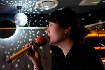 side view of one Asian young woman holding microphone, singing karaoke in KTV
