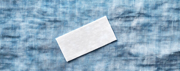 A close-up of a blank white laundry care label attached to blue textured fabric with a natural brown twine, showcasing minimalist design and soft textile details.
