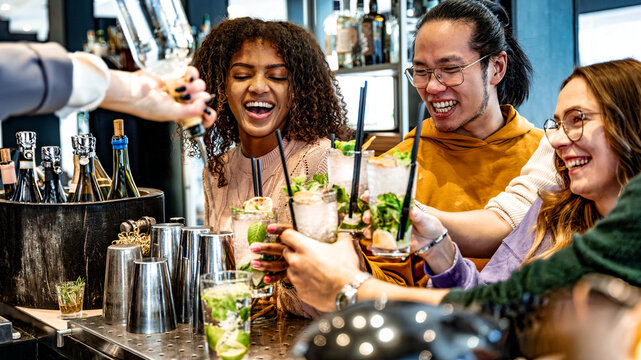 Bartender lady pouring alcohol from the bottle into the glasses - Happy friends group cheering mojito glasses on weekend night at cocktail bar venue - Life style concept with barman making drinks