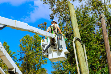Technician handles wiring on power pole using lift, set against home