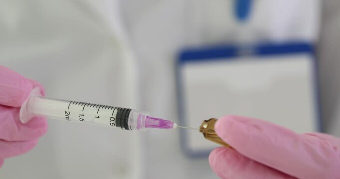 Assistant in pink gloves fills syringe with vaccine from glass vial in clinic. Medical worker prepares medication for injection in hospital office