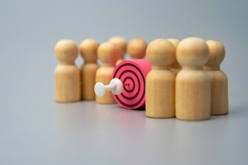 A target with a dart in the center surrounded by wooden figures. Target customer concept.