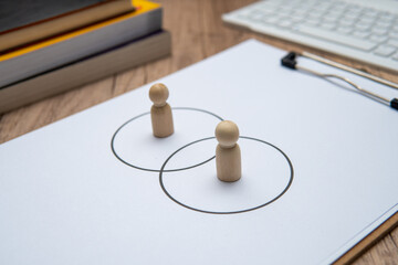 Two wooden figures standing in separate circles overlaps with each other. Consensus and agreement...