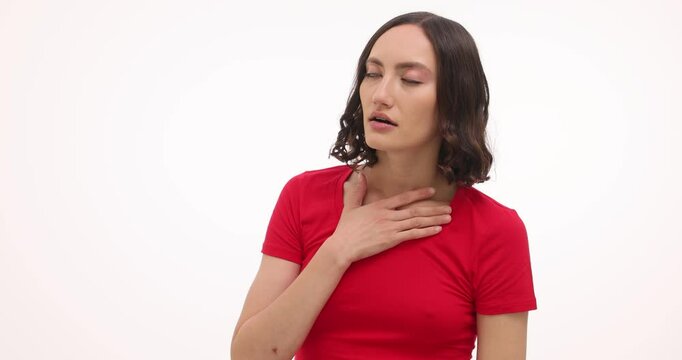 Brunette woman with breathing problems holds chest with palms on white background. Young female in red t-shirt suffocates from disease attack