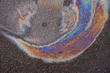 A colorful oil slick spreading across an asphalt surface