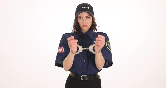 Sad woman police officer raises hands with handcuffs on wrists. Brunette lady cop in uniform faces arrest for accepting bribe on white background