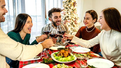 Millennial people toasting red wine at home supper Christmas party - New year's eve and winter holiday concept with young friends having fun eating together at evening