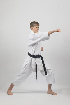 Fifteen year old male teenage karate black belt in long stance doing a head punch, studio shot against a white background