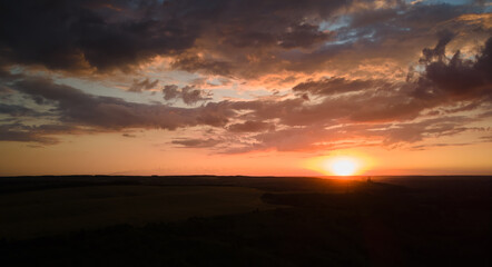Bright colorful sunset sky with setting sun and vibrant clouds over dark landscape