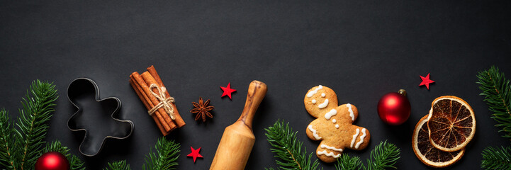 Christmas food and ingredients for cooking at black. Gingerbread cookies, spices and Christmas decorations. Web banner format.