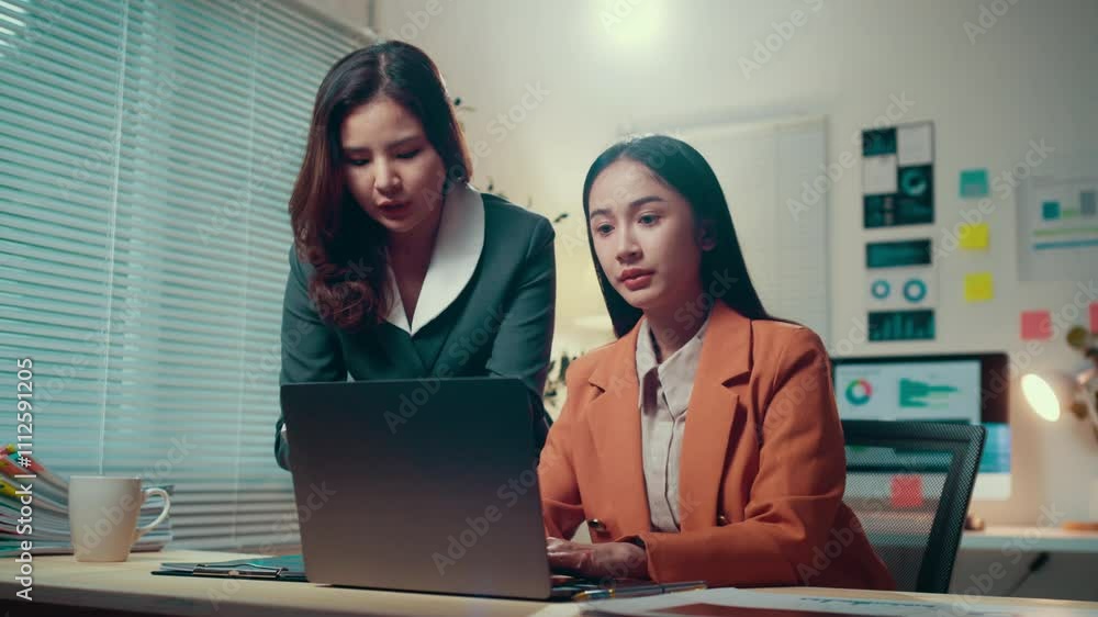 Poster two businesswomen work late at night in the office, discussing projects and analyzing data on a lapt