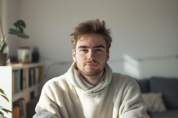 Portrait of a content man in his 20s dressed in a comfy fleece pullover while standing against modern minimalist interior