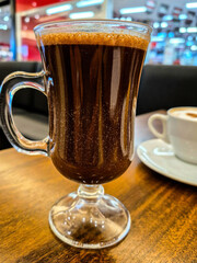 Close up em uma caneca de vidro com chocolate quente, sobre uma mesa de madeira em uma cafeteria no shopping.