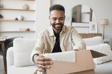 Happy man opening parcel at home, handsome guy opens package indoor, delivery, shipment, satisfied...