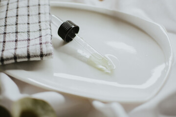 Pipette from a brown cosmetic jar for serum close-up on a white saucer with a towel and eucalyptus