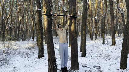 Strong and muscular man exercising on horizontal bar at winter nature. Handsome guy doing pull ups...