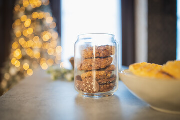 Cookies with chocolate and cinnamon in a glass jar, standing on the white kitchen countertop. Garlands. Light. Home comfort. Christmas homemade cookies