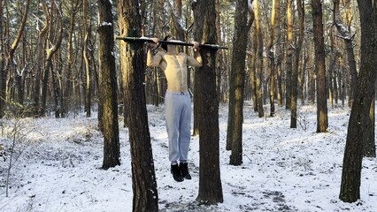Strong and muscular man exercising on horizontal bar at winter nature. Handsome guy doing pull ups...