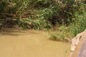 Jordan. Place of Jesus' baptism. Muddy water in Jordan River bed near baptism site. Close-up of wooden flooring of place where tourists dive. Holy Land is fifth Gospel