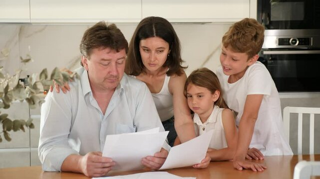Worried adult man examining documents at table with family