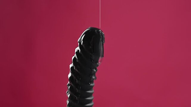 Lube pouring on black dildo on pink background. 