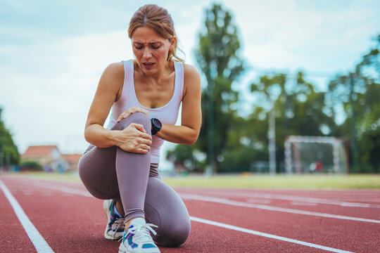 Woman Experiencing Knee Pain on Outdoor Running Track in Summer
