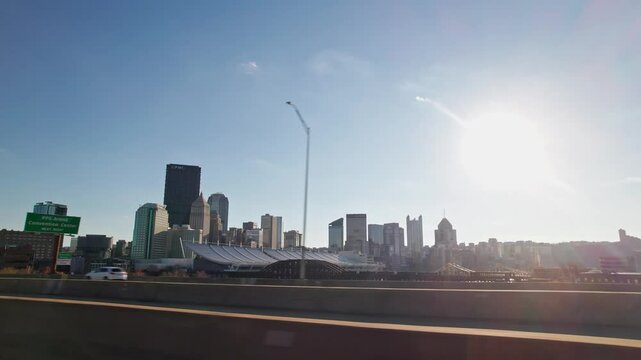 Car driver pov and perspective moving past Pittsburgh Pennsylvania city skyline, buildings, skyscrapers, business, and residential urban district looking out window from highway and interstate road
