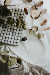 Pipette from a brown cosmetic jar for serum close-up on a white saucer with a towel and eucalyptus