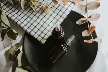 Brown cosmetic jars with pipette for serum close-up on a black plate with a towel and eucalyptus