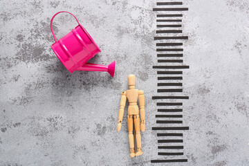 Composition with watering can, wooden mannequin and height measurements on grunge background