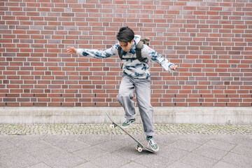 Teenage girl with backpack doing skateboard tricks while riding down the street