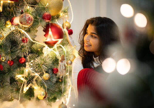 Indian woman celebrating Christmas festival, beautiful girl sitting near Christmas tree - Powered by Adobe