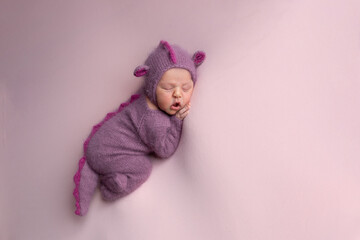 Little adorable newborn baby girl sleeping in a hat with dragon ears. Neutral background. Studio shot of a ten-day-old newborn baby. Beginning of life. Fairy tale. Dragon toy