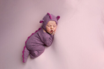 Little adorable newborn baby girl sleeping in a hat with dragon ears. Neutral background. Studio shot of a ten-day-old newborn baby. Beginning of life. Fairy tale. Dragon toy