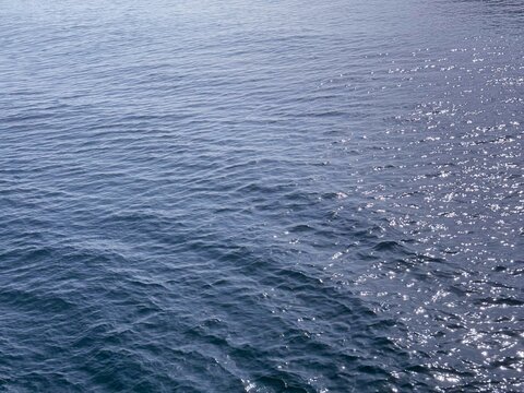 Blue sea water surface with sun reflections.